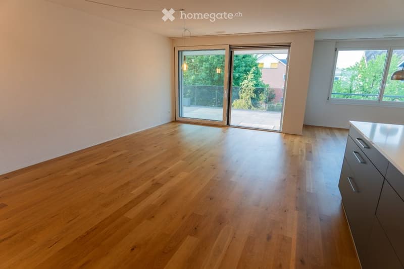 Empty room with wooden flooring, large sliding glass doors leading to a balcony, and white walls.
