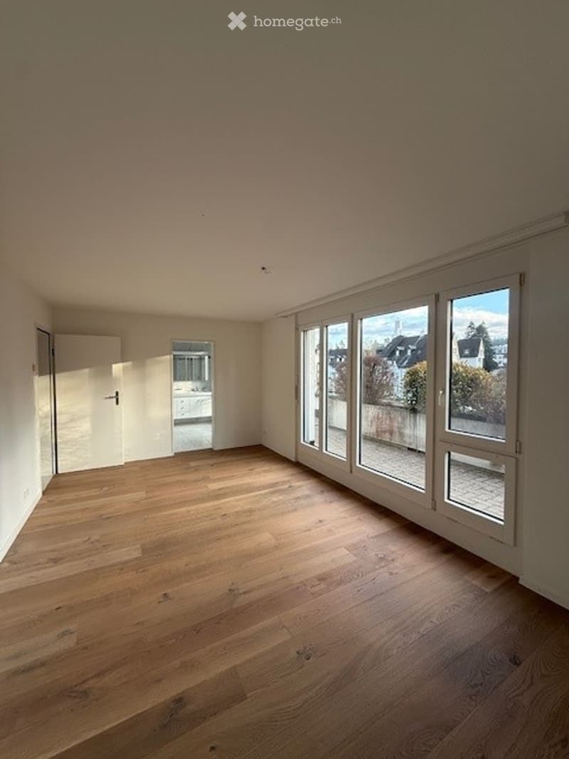 Completely empty room with wooden flooring, large windows, and white walls.