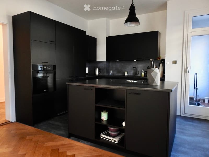 Modern kitchen with black cabinets, stainless steel appliances, and a central island with open shelving. Includes a sink, faucet, and decorative vase on the counter.