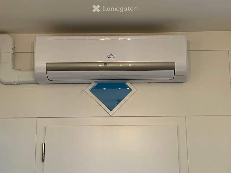 A modern white air conditioner unit mounted on a light-colored wall above a cabinet.