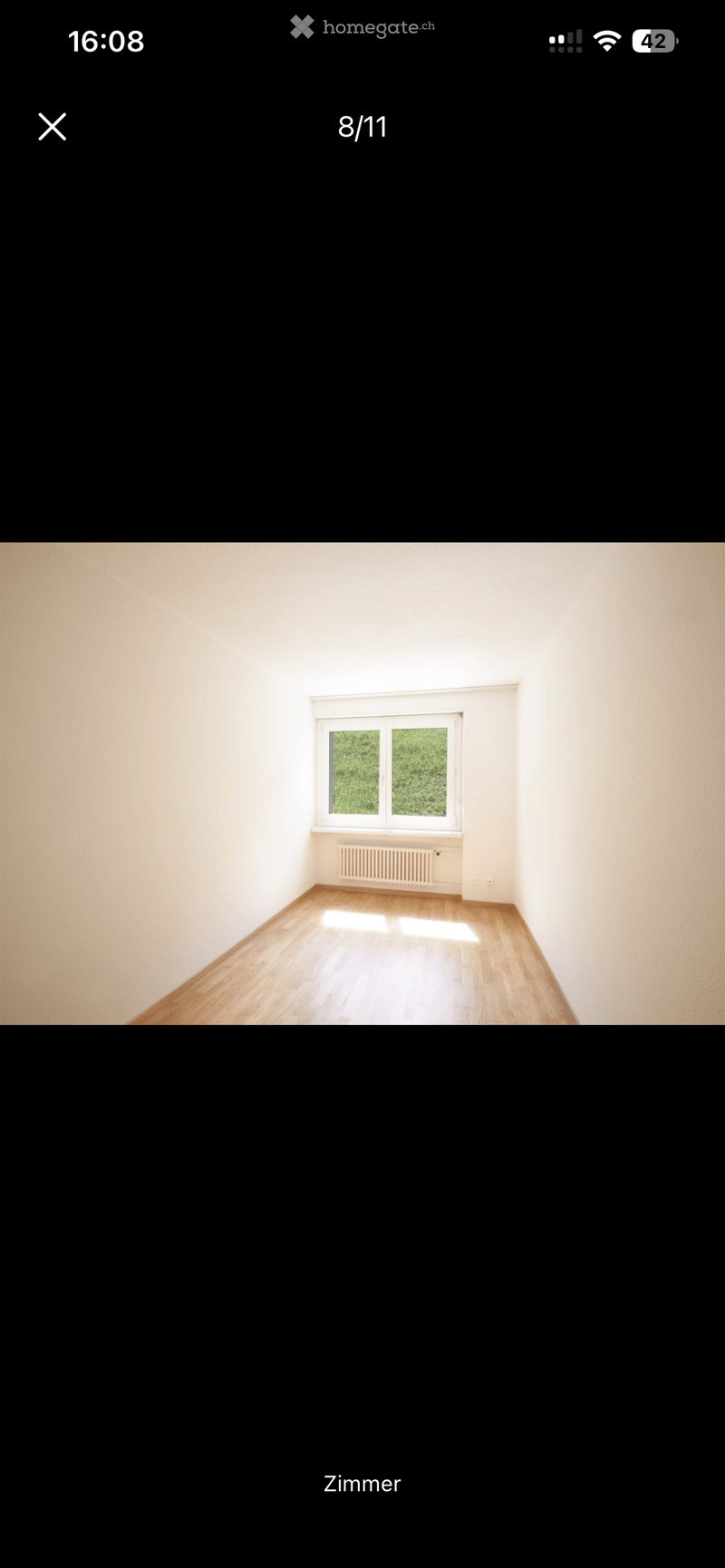 Empty room with wooden flooring, white walls, and a single window with a radiator below it.