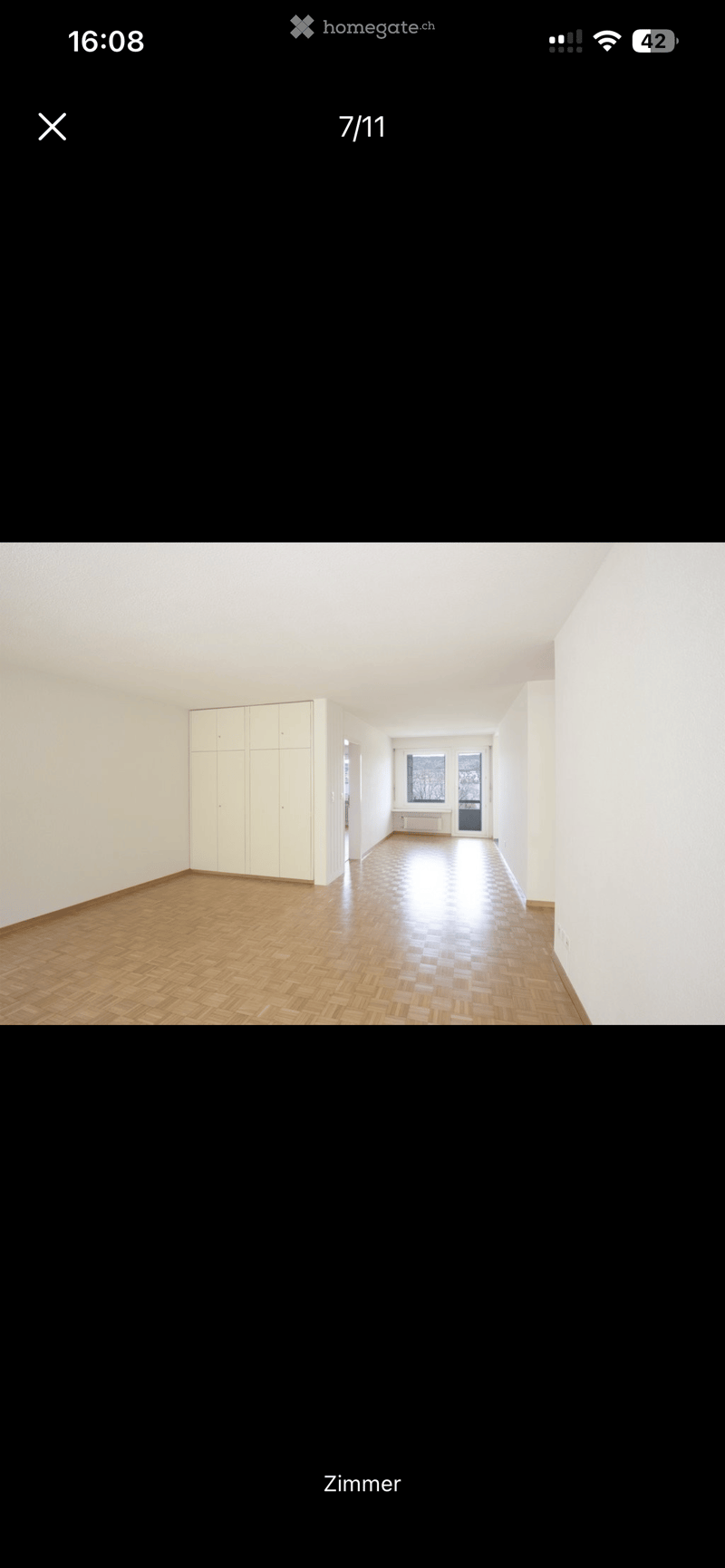 Empty room with wooden flooring, white walls, and a built-in closet. Natural light from a window at the far end.