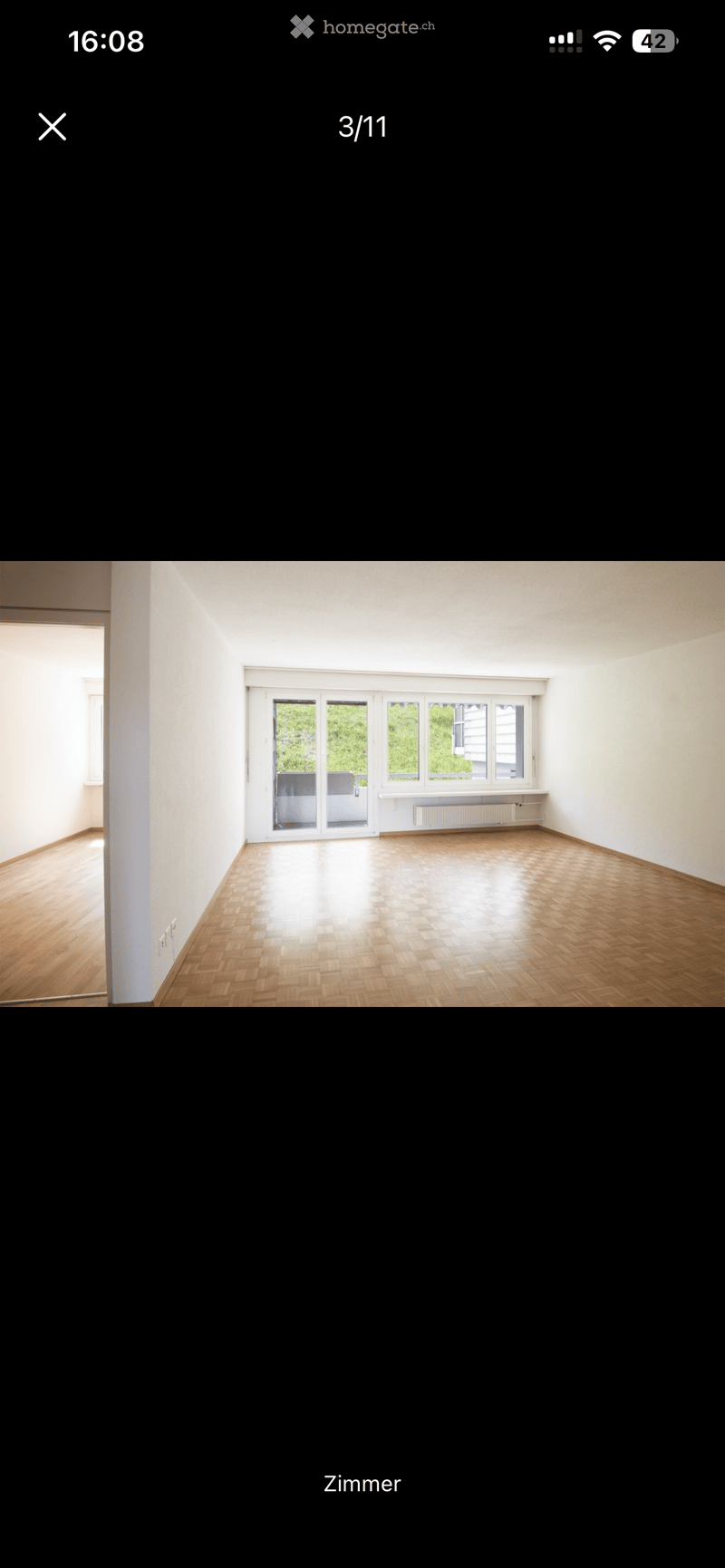 Empty room with wooden flooring, white walls, large windows, and a sliding glass door leading to a balcony.