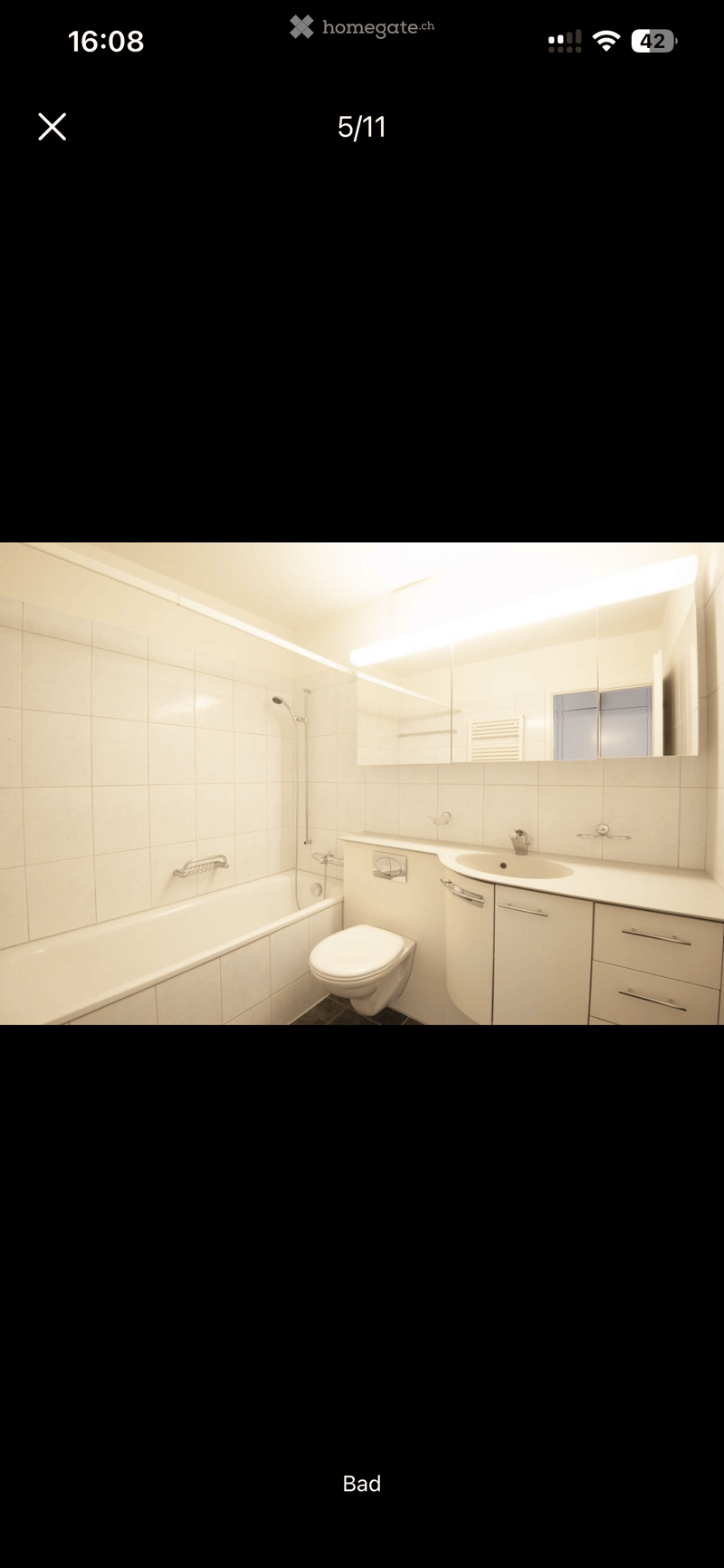 Modern bathroom with white tiles, a bathtub, toilet, sink, and mirrored cabinet.