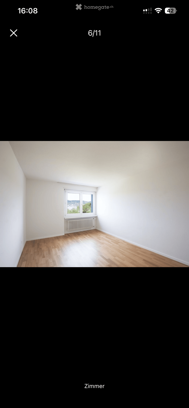 Empty room with wooden flooring, white walls, and a single window with a radiator below it.