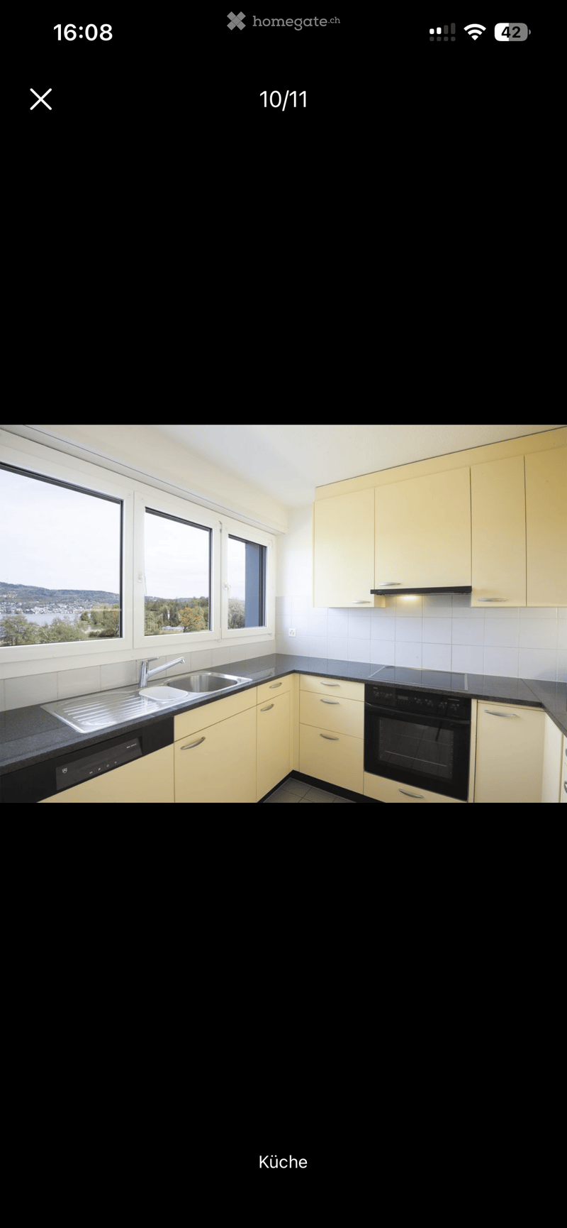 Modern kitchen with light-colored cabinets, black countertops, stainless steel sink, and built-in appliances including an oven and dishwasher. Large windows offer a scenic view.