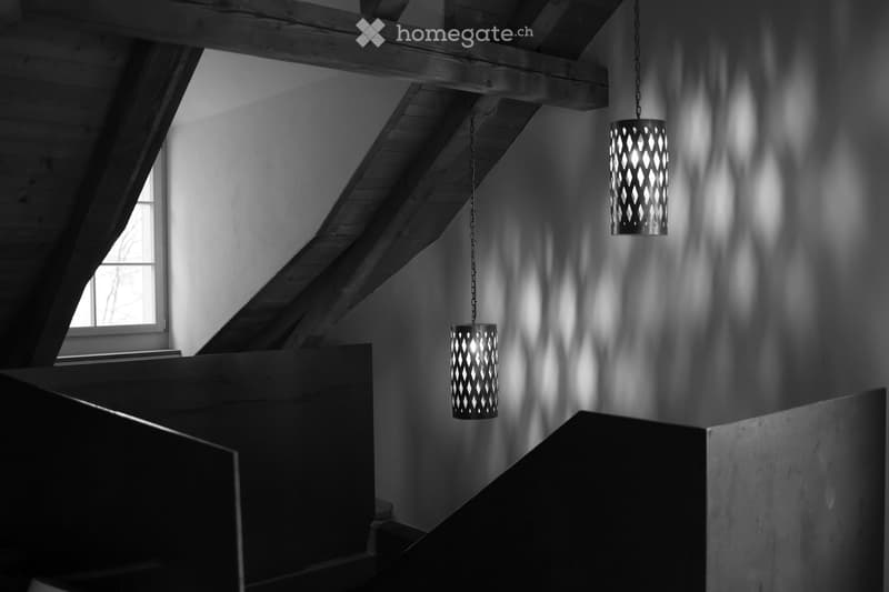 Staircase with exposed wooden beams and geometric patterned pendant lights casting shadows on the walls.