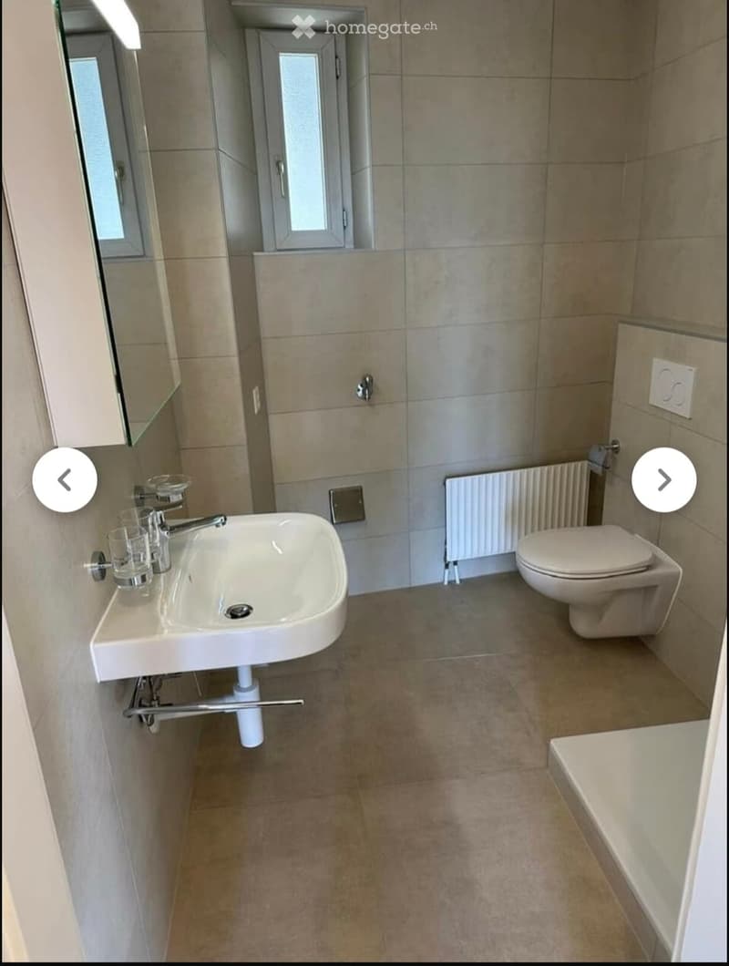 Modern bathroom with beige tiles, a white sink, a toilet, a bathtub, a radiator, and a mirror above the sink.
