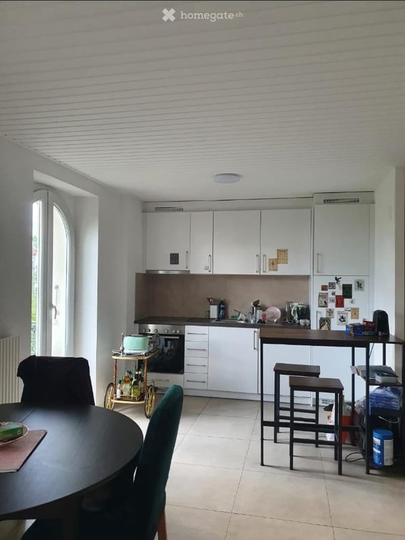 Modern kitchen with white cabinets, stainless steel appliances, a central island with stools, and a dining area with a round table and chairs.