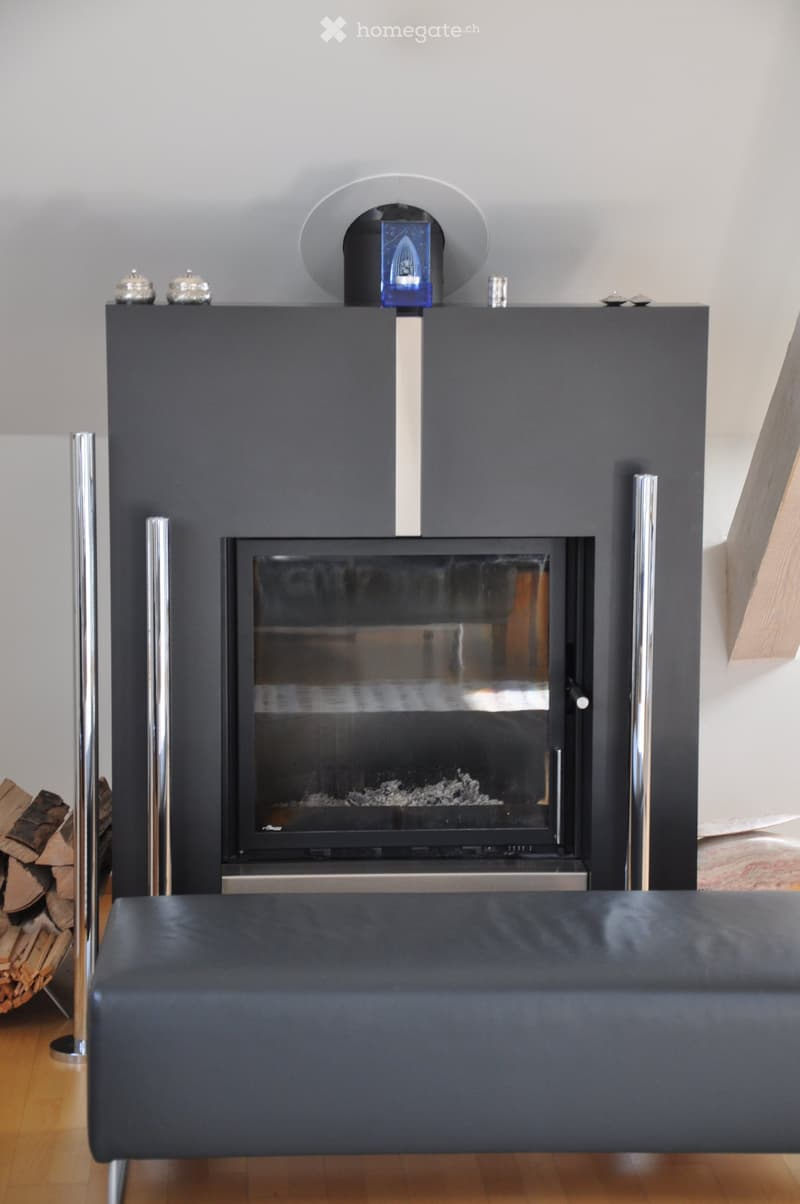 Modern living room with a sleek black fireplace, a dark leather stool, and a stack of firewood to the left.