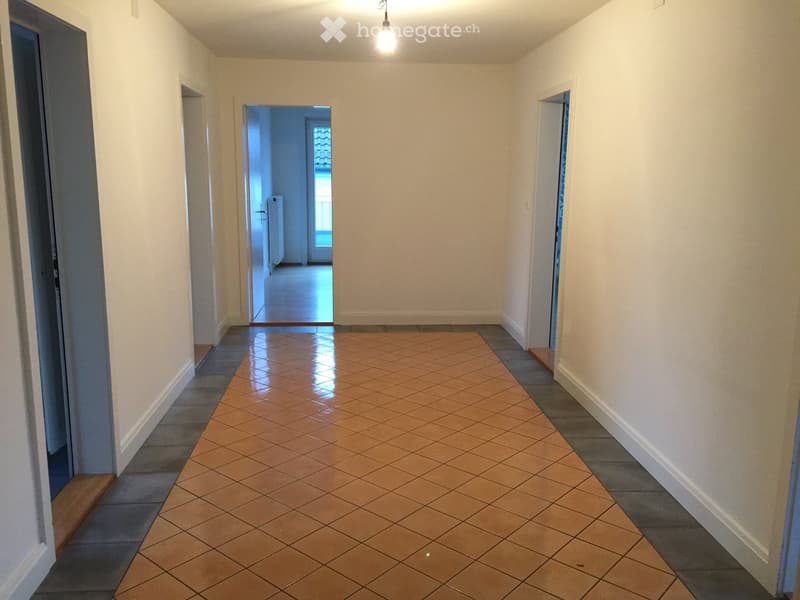 Empty hallway with tiled floor and white walls, featuring several doors and a visible room at the end.