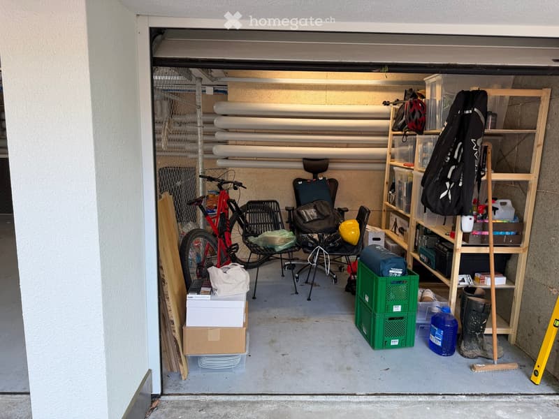 Garage with bicycle, chair, shelf, backpack, helmet, crate, bottle, boots, mop, and level.