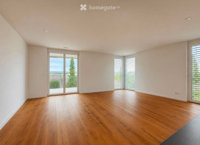 Empty room with wooden flooring, white walls, large sliding glass doors leading to a balcony, and multiple windows with blinds.