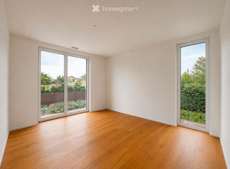 Empty room with wooden flooring, white walls, and large sliding glass doors opening to a garden area.