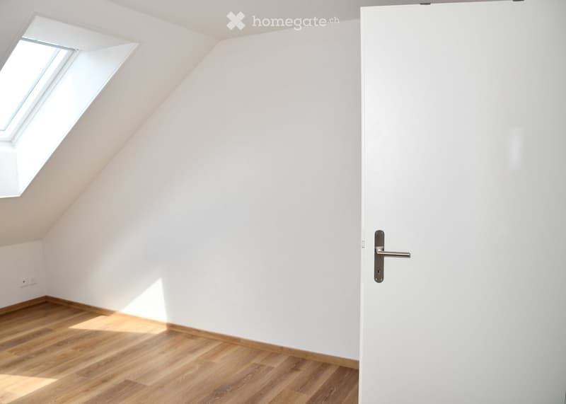 Empty attic room with wooden flooring, white walls, and a skylight window providing natural light.