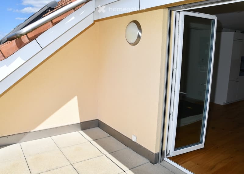 Balcony with beige tiled floor, light-colored walls, and a sliding glass door leading to an interior space. A round mirror is mounted on the wall.