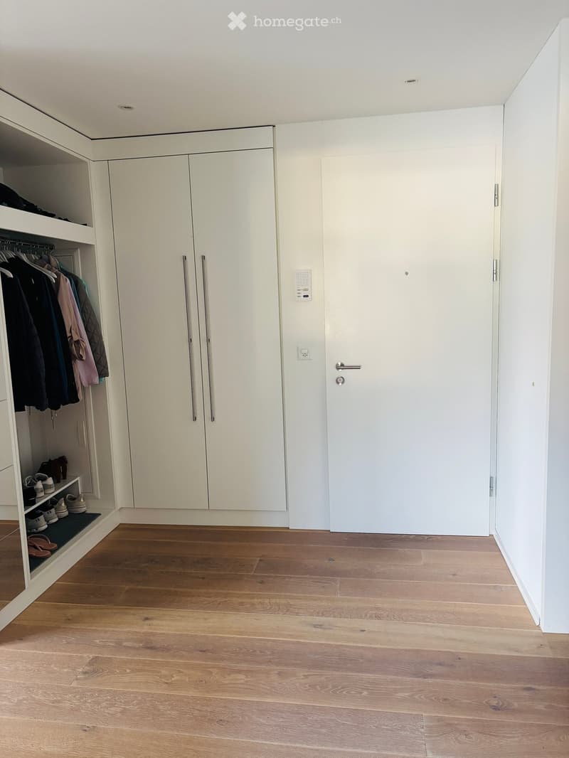 Empty room with light wooden flooring, white walls, built-in closet with shelves and hanging space, and a closed door.