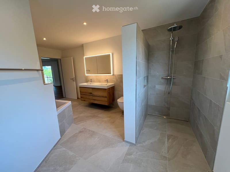 Modern bathroom with a double sink, wooden vanity, large mirror with LED lighting, separate shower area with glass enclosure, and a bathtub.
