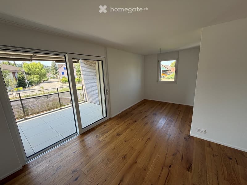Empty room with wooden flooring, large sliding glass door leading to a balcony, and a window on the adjacent wall.