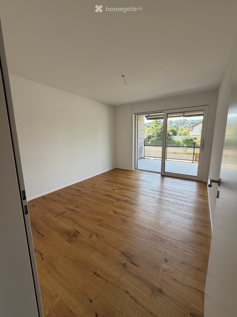 Empty room with wooden flooring, white walls, and large sliding glass doors leading to a balcony.