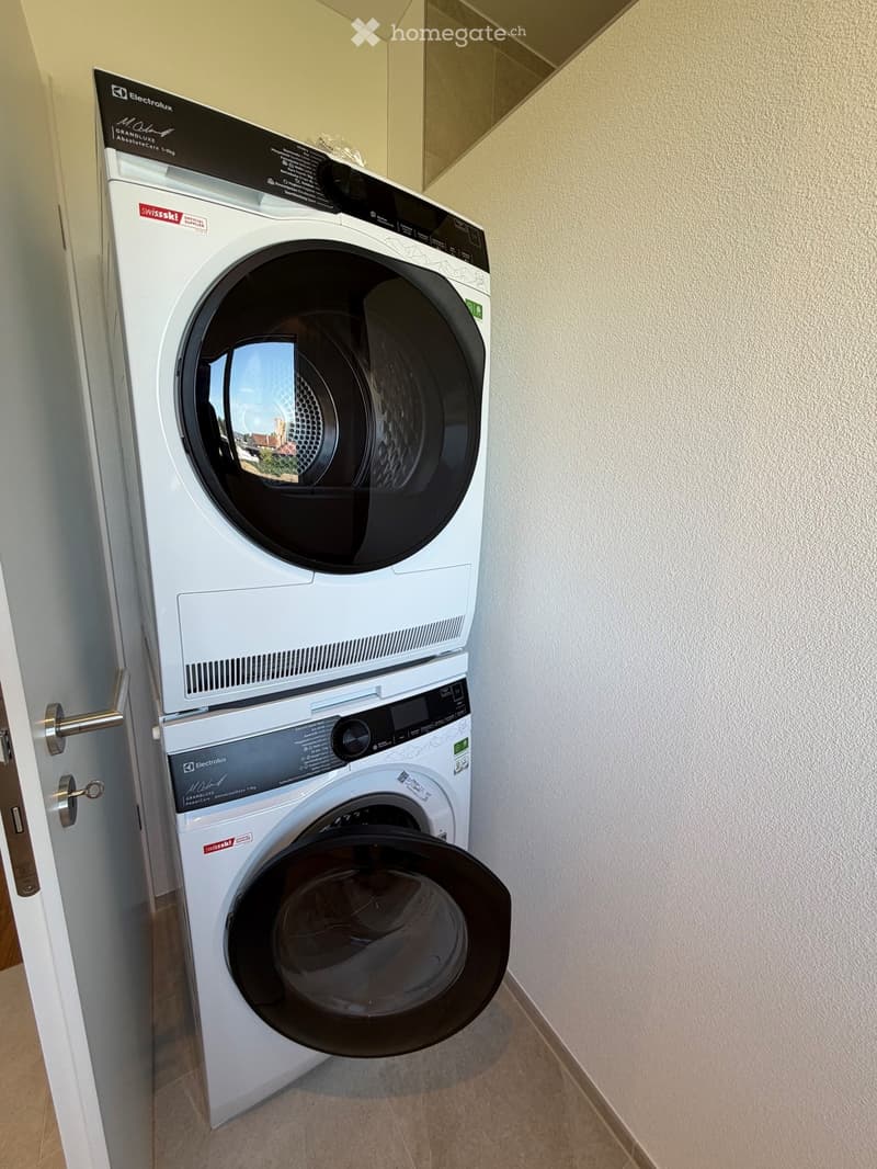 A compact bathroom with a stacked washing machine and dryer unit, featuring a sleek white design and modern control panels.