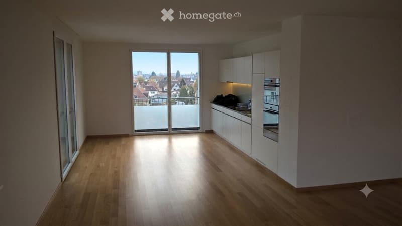 Bright, open-plan kitchen and living space with wooden flooring, white cabinets, and a large window offering a view of the cityscape.
