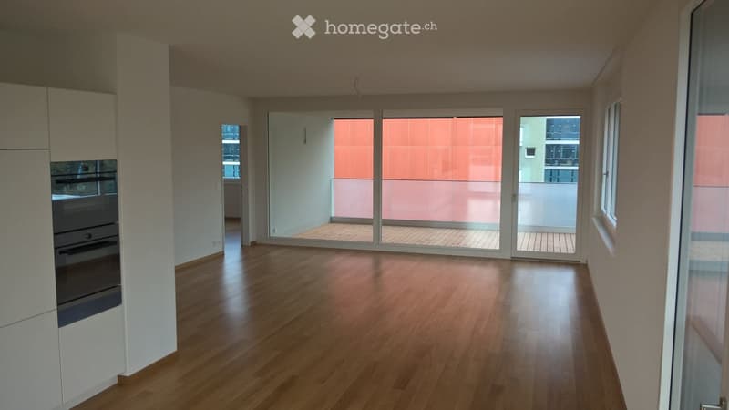 Empty room with wooden flooring, large sliding glass doors leading to a balcony, and a built-in oven unit on the left side.