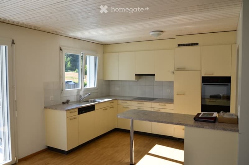 Bright kitchen with light yellow cabinets, granite countertop, sink, dishwasher, and oven. Wooden flooring and large windows provide natural light.