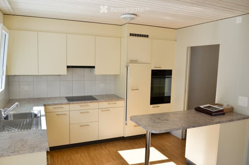Modern kitchen with light-colored cabinets, granite countertops, stainless steel sink, stove, and oven. Wooden flooring and white walls.