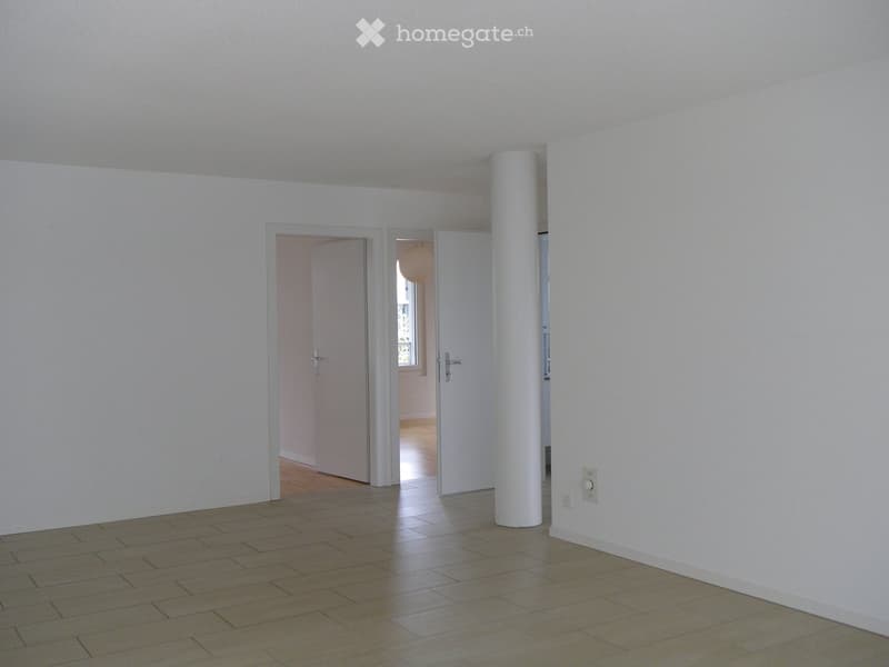 Empty room with light-colored walls, wooden flooring, and two open doors leading to adjacent spaces.