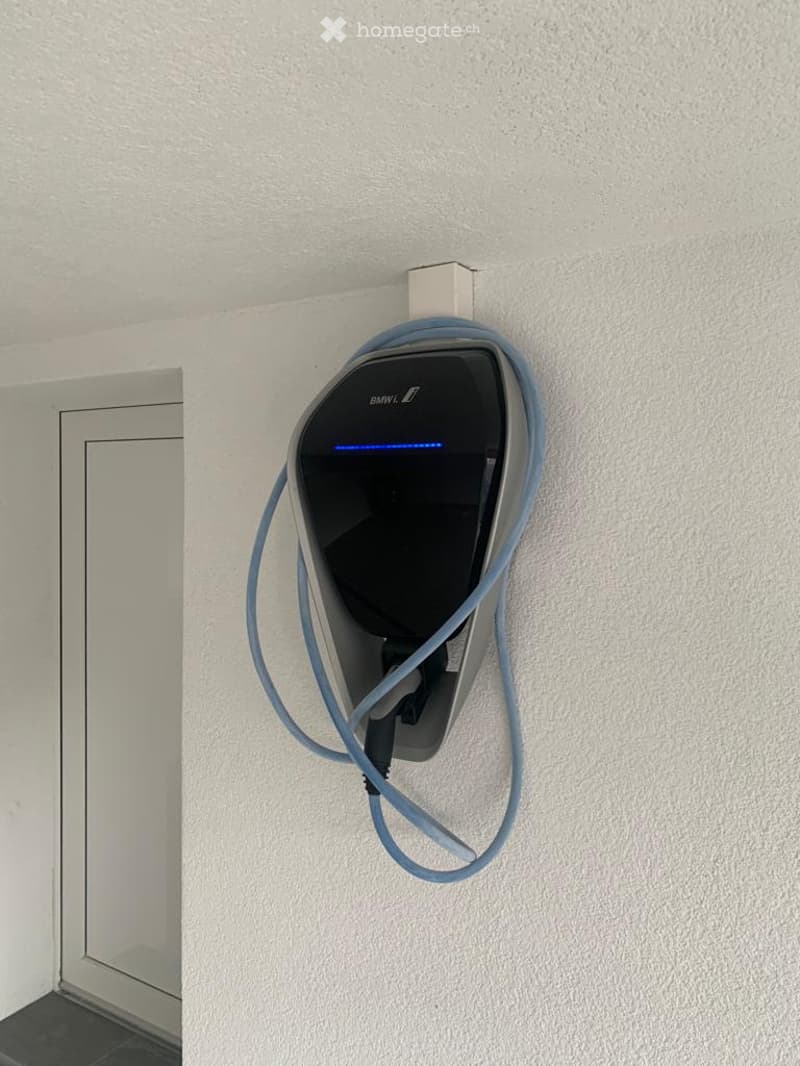 A BMW-branded electric vehicle charging station mounted on a white wall, with a blue cable connected.