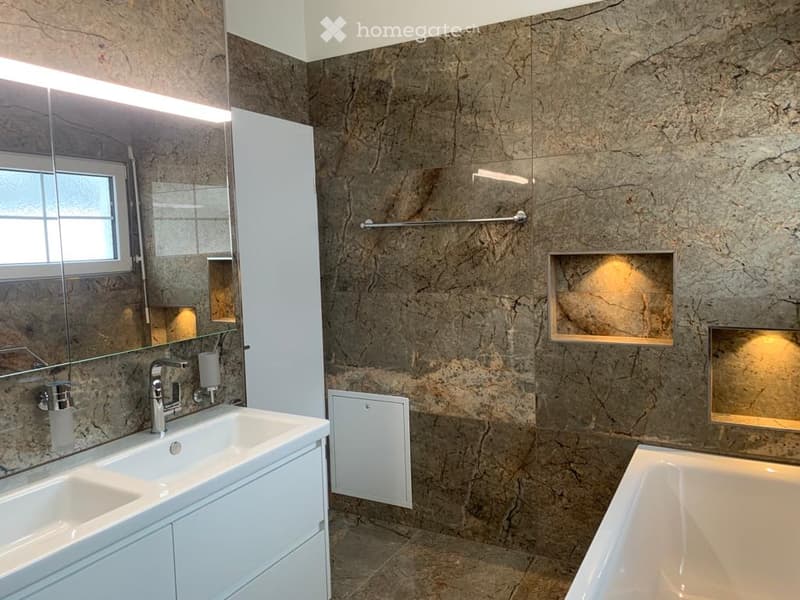 Modern bathroom with marble walls, a double sink, a bathtub, a large mirror, and built-in shelves.