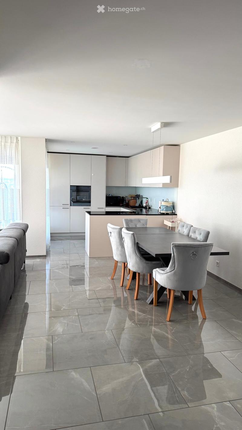 Modern dining area with a sleek black dining table and six upholstered chairs, adjacent to a contemporary kitchen with white cabinets, stainless steel appliances, and a polished tile floor.