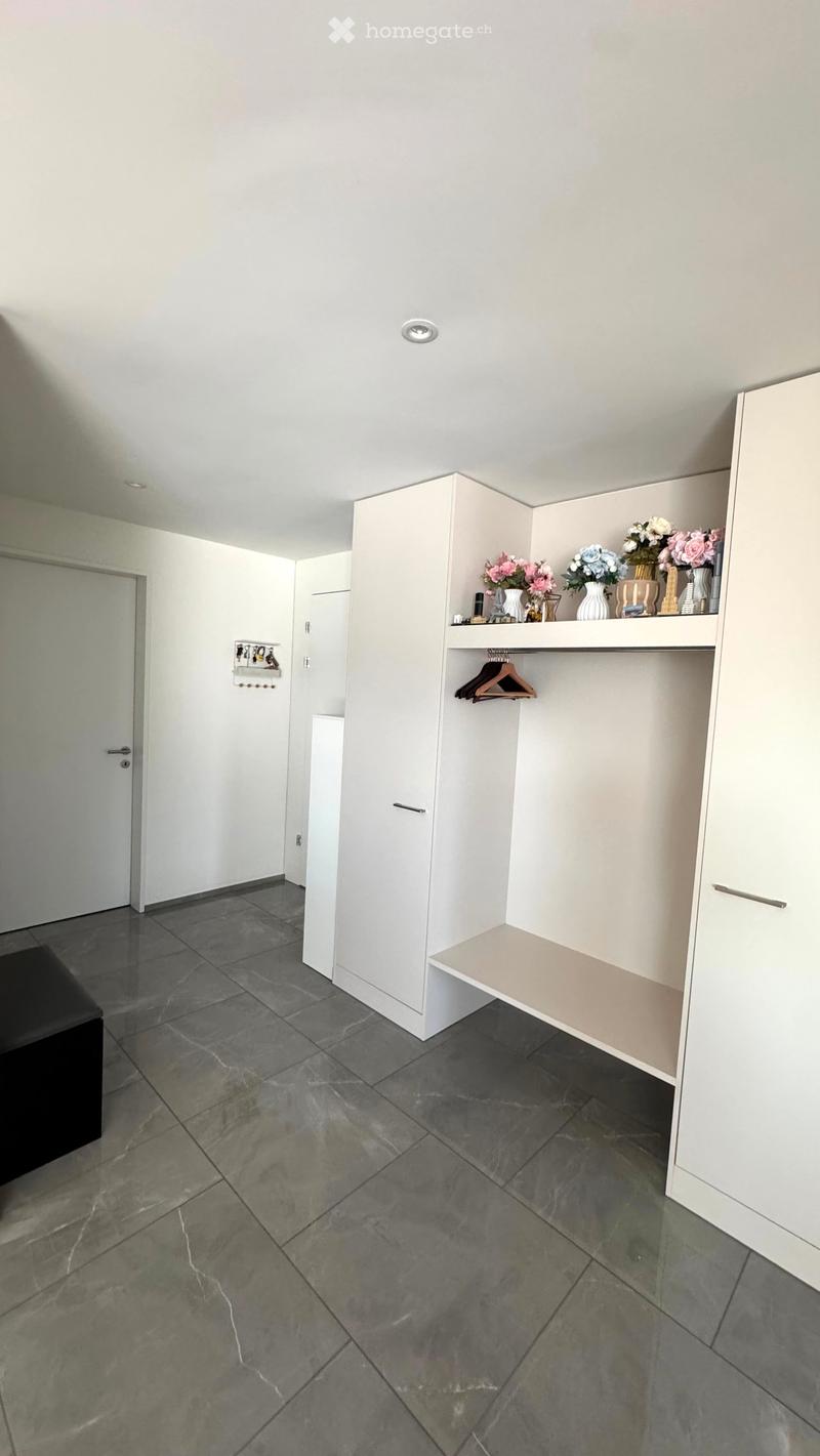 A modern, minimalist walk-in closet with white built-in wardrobes, grey marble flooring, and decorative vases with flowers on the shelves.