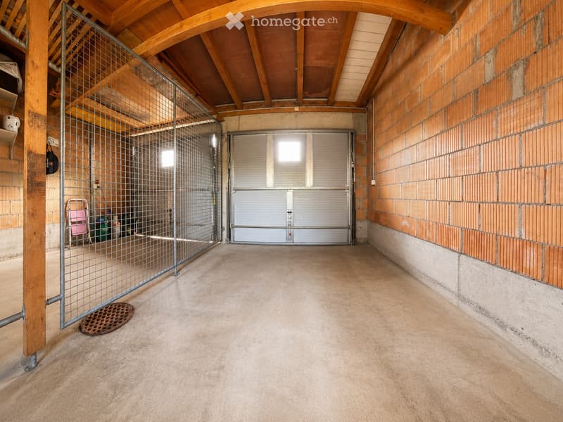 Empty garage with wooden beams, metal gate, and concrete floor.