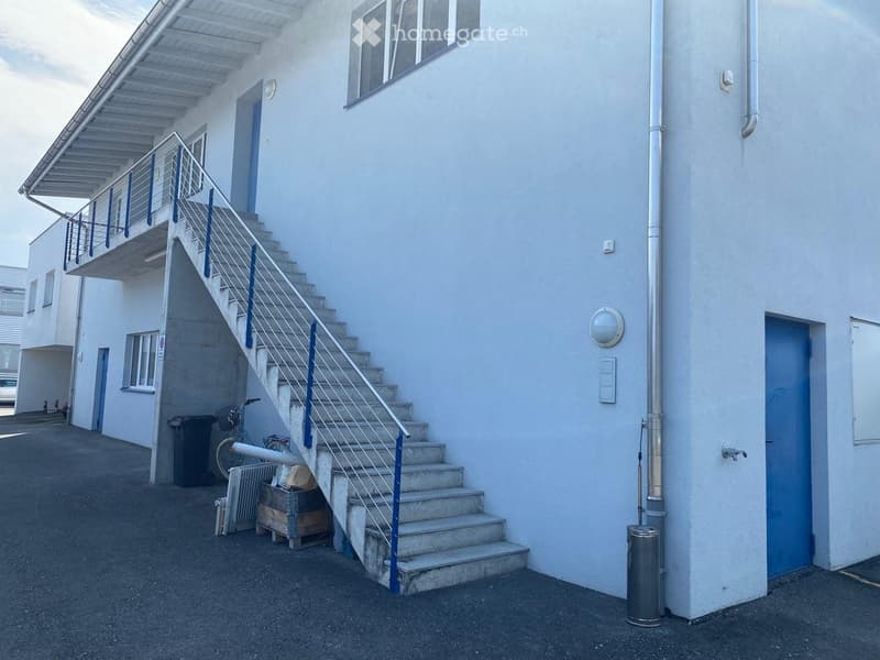 Exterior view of a two-story building with a staircase leading to an upper level, featuring a metal railing and blue doors.