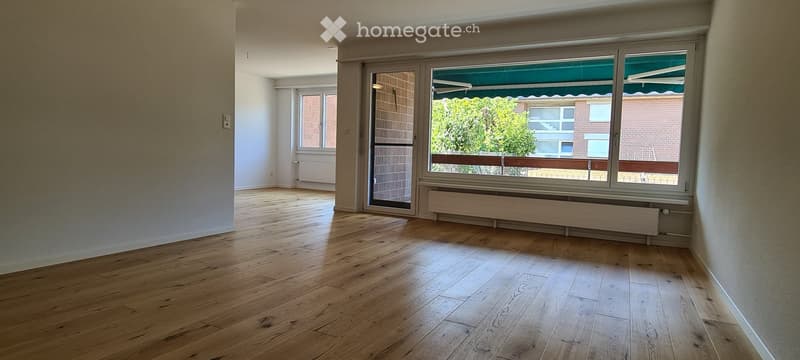 Empty room with wooden flooring, large windows, and a sliding door leading to a balcony.