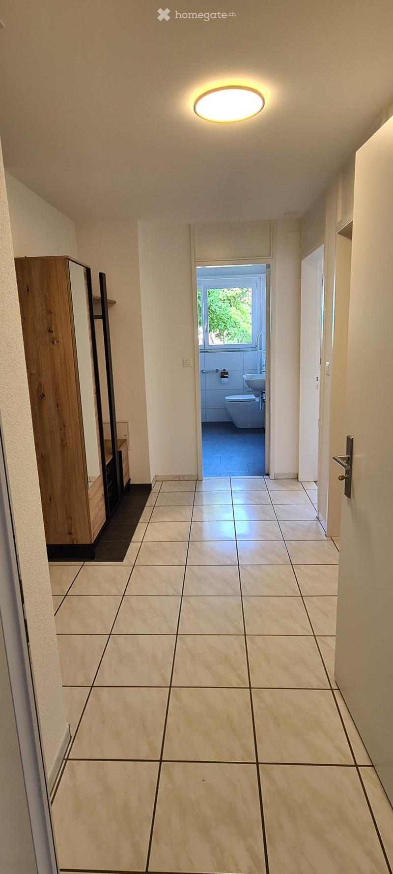 Clean hallway with tiled floor, recessed lighting, and a partially visible bathroom at the end.