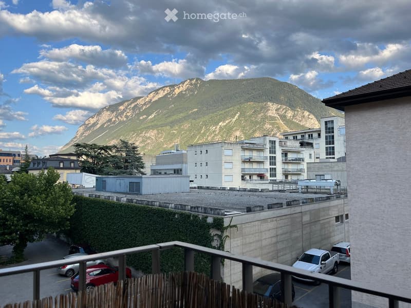 Balcony overlooking a parking lot and surrounding buildings, with a mountain view in the background.