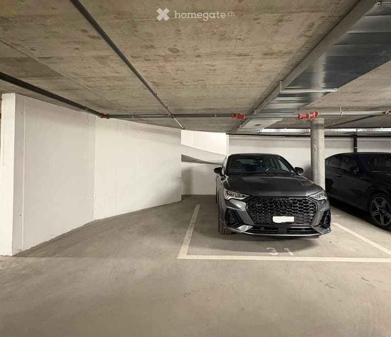 Underground parking area with two parked cars, marked parking spaces, and concrete pillars.