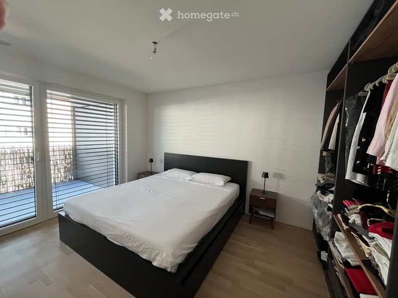 Modern bedroom with a large bed, nightstands, wardrobe, and large windows with blinds.