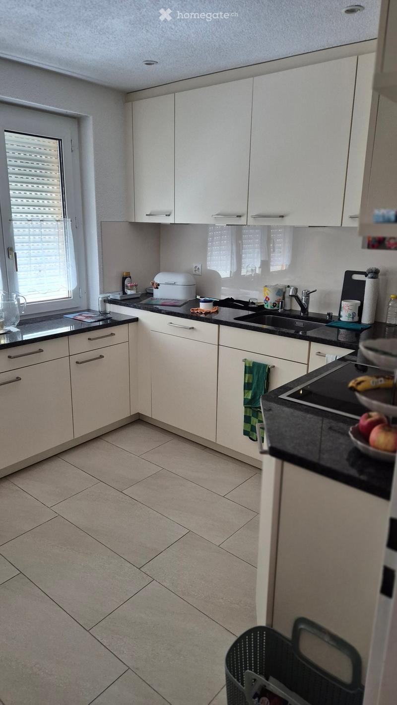 Modern kitchen with white cabinets, black countertops, and tiled floor. Features a sink, faucet, oven, toaster, and various kitchen items on the counters.