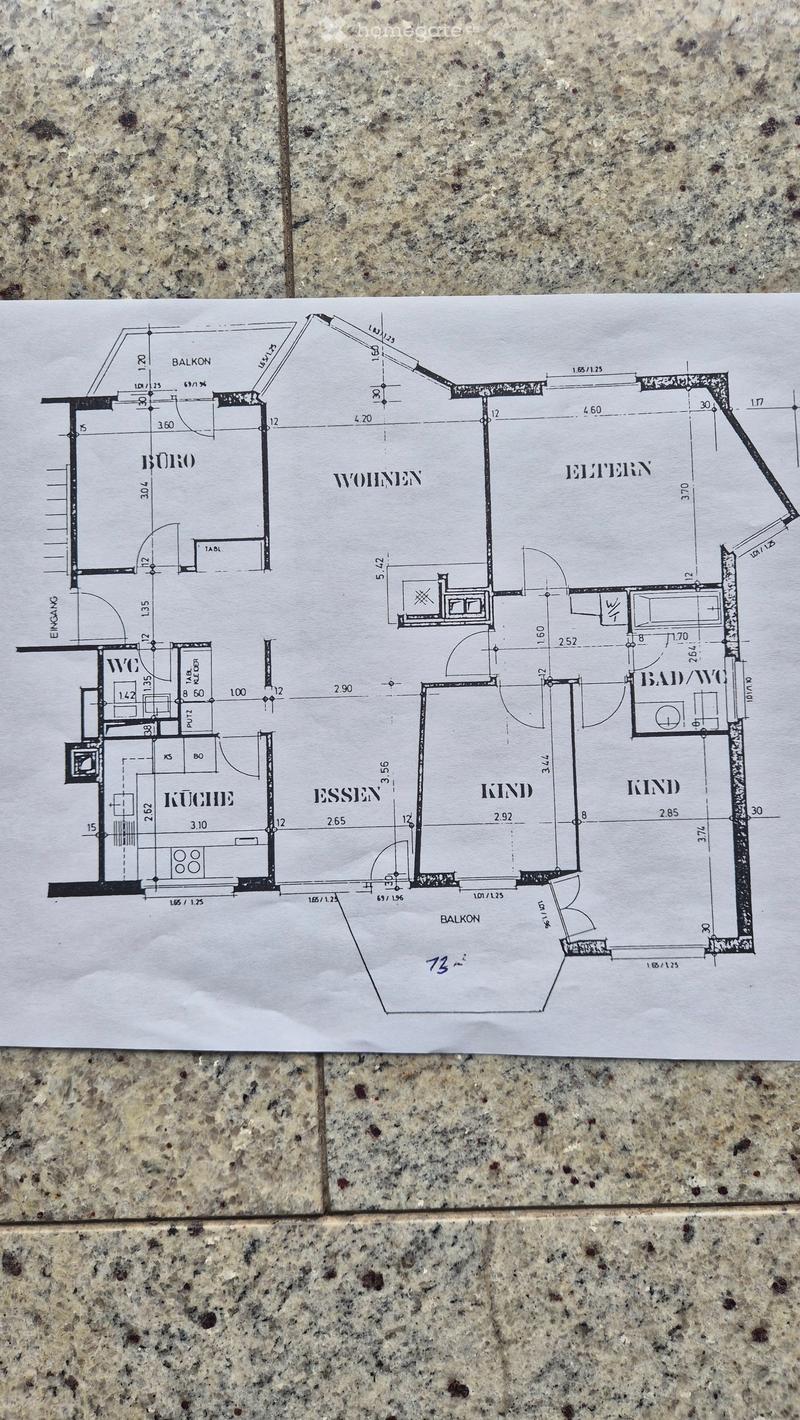 Floor plan showing a layout with rooms labeled in German: WOHNEN (living), ESSEN (dining), KÜCHE (kitchen), BAD/WC (bathroom), WOHNEN (office), and two KIND (children's rooms). Includes two balconies.