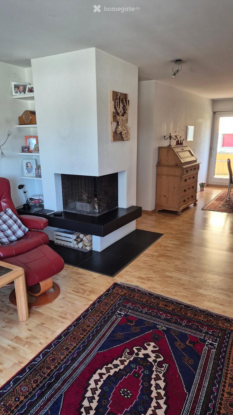 Living room with a fireplace, red leather sofa, wooden table, and decorative items on shelves.