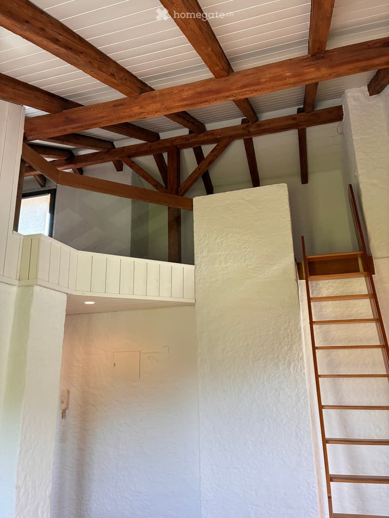 Staircase with wooden steps and handrails, white textured walls, exposed wooden beams on the ceiling, small window, and built-in white cabinetry above the stairs.