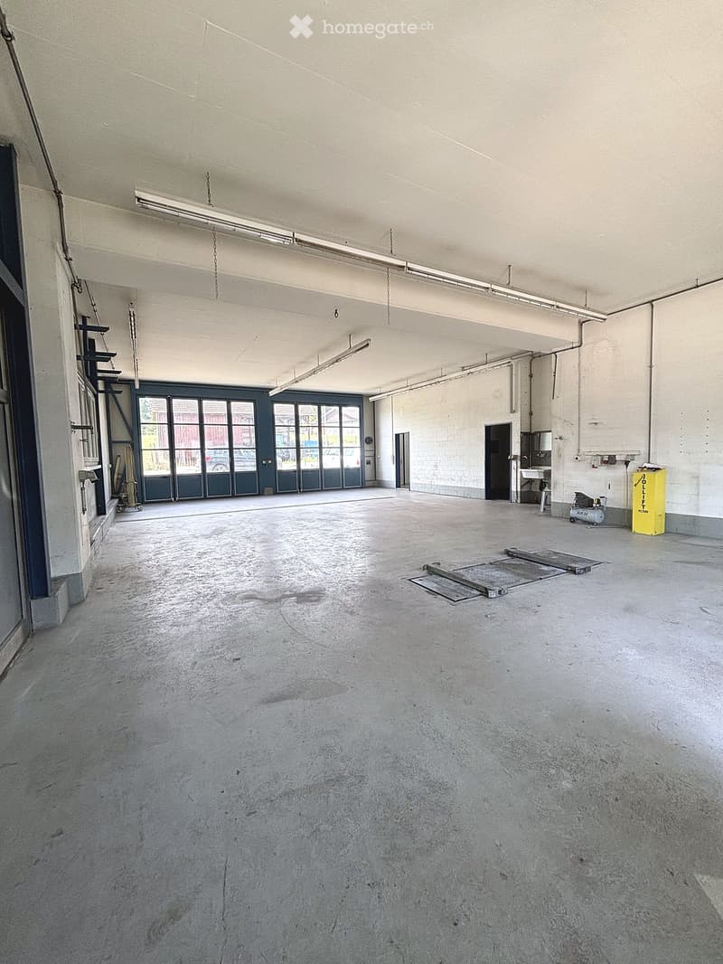 Empty industrial-style room with concrete floor, large windows, and minimal fixtures including a sink and a yellow container.