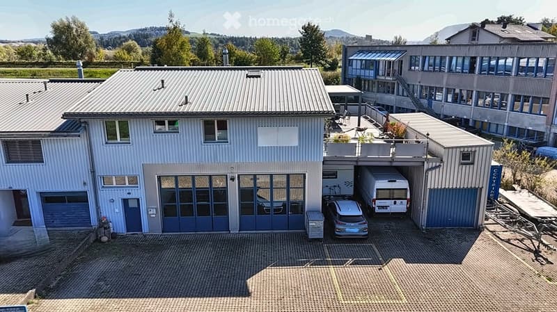 Two-story building with a garage, multiple windows, and a parking area with a van and car.