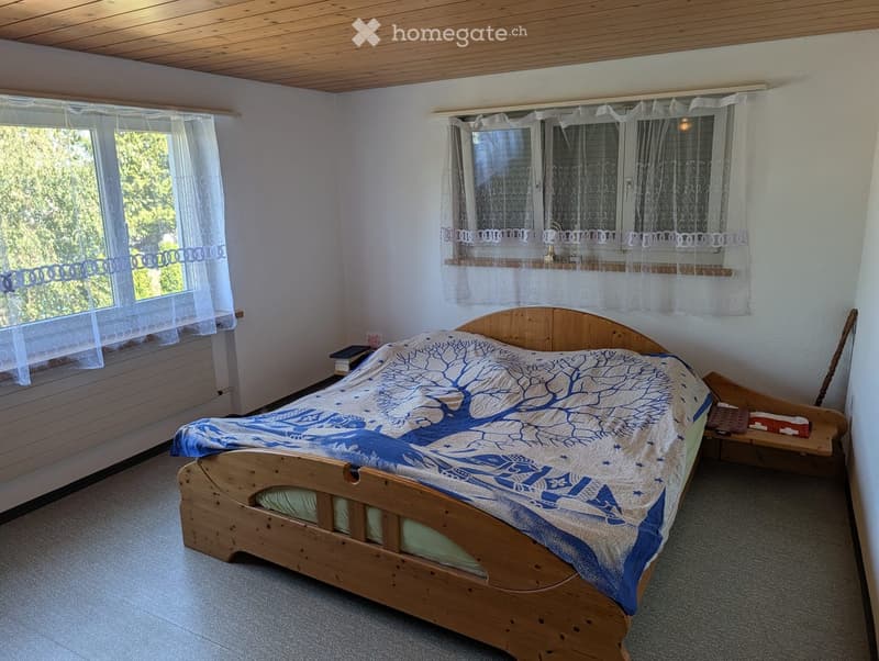 Cozy bedroom with a wooden bed, blue and white patterned bedspread, nightstand, and books on the windowsill.