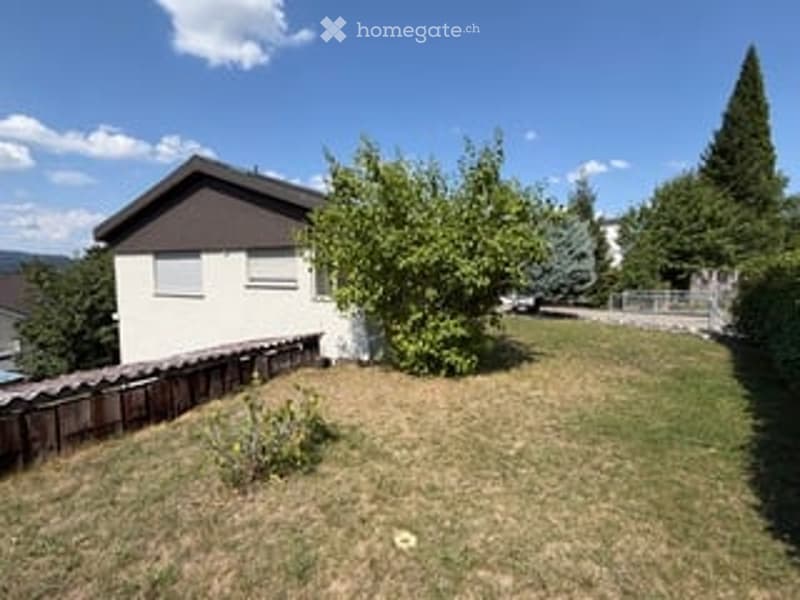 Front yard of a house with a wooden fence, a tree, and a parked car in the background.