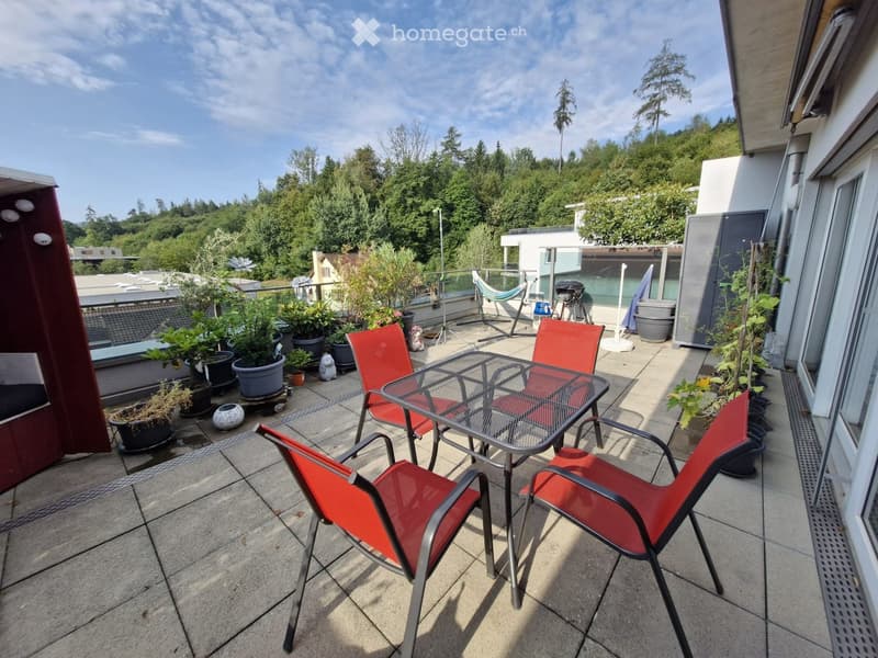 Balcony with a glass table, red chairs, potted plants, and a view of greenery.